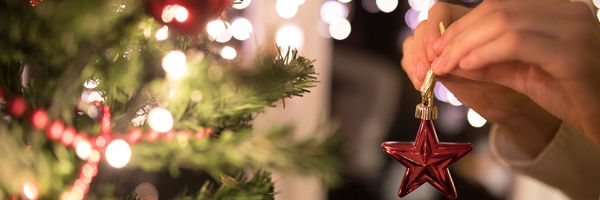 two hands hanging a red star ornament on a tree